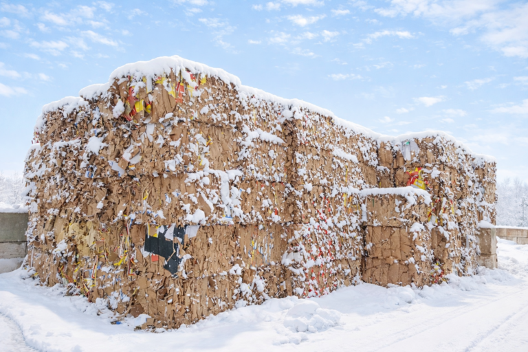 Große Stapel von zerknittertem Karton, teilweise mit bunten Papierresten, bedeckt mit Schnee im Freien